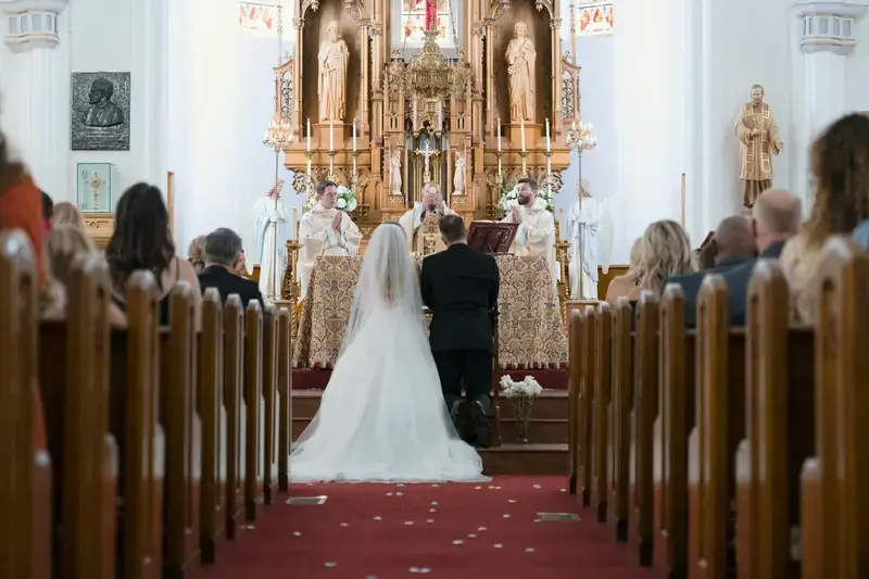 A bride in white walking up the aisle of a church with wooden pews