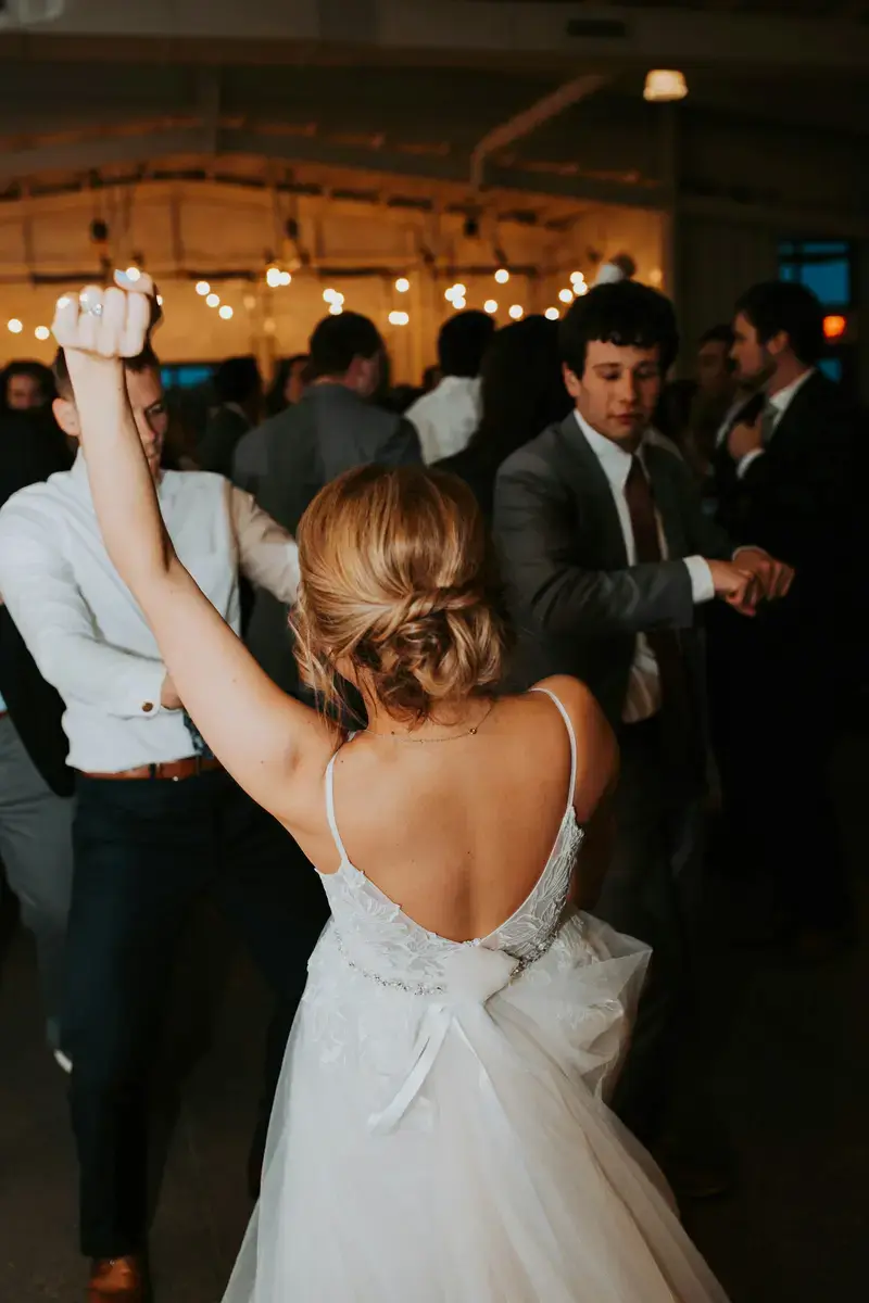 A bride in a white dress dancing with guests at a candle-lit reception